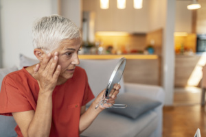 Senior woman looking at her skin in the mirror before her HALO Fractional Laser Treatment in Austin, TX