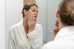 Woman in bathrobe looking in mirror at bathroom after her HALO Fractional Laser treatment in Austin, TX