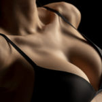 Woman with perfect breasts in black bra on black background