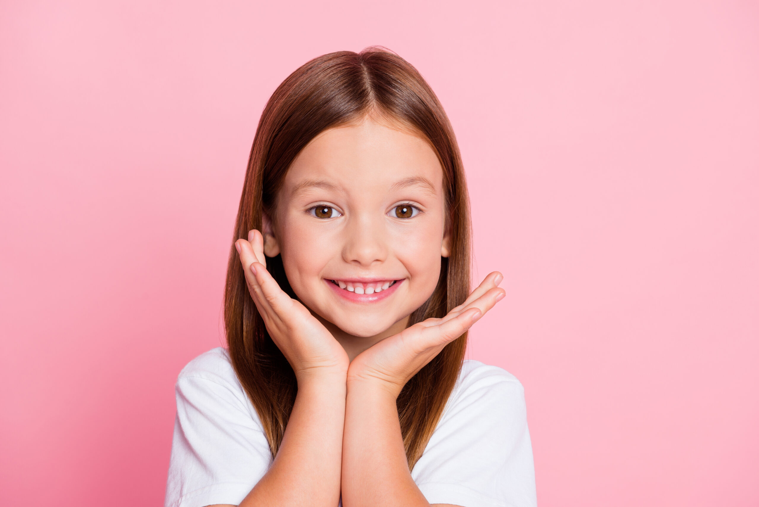 A young girl smiling with her hands framing her face