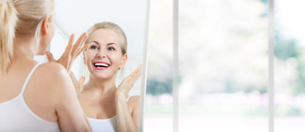 Woman looking in the mirror smiling at her youthful look from a facelift in Austin, TX