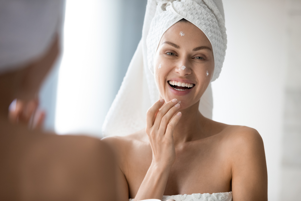 Woman smiling in the mirror putting on moisturizer after NanoLaserPeel in Austin, TX